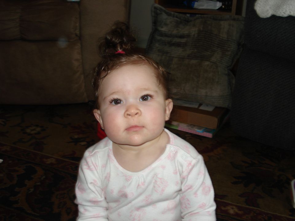 Baby girl with hair in a bun, wearing a pink and white patterned onesie
