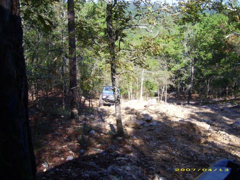 1978 Ford Bronco - Two off-road vehicles navigate a challenging, sun-dappled path through a dense forest.