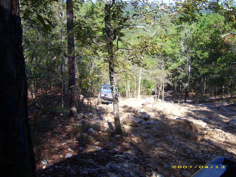 Light blue off-road vehicle driving on a rocky, wooded trail