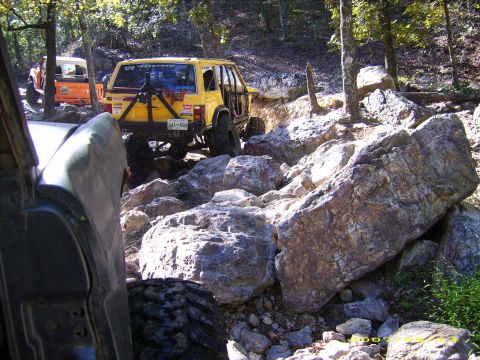 1978 Ford Bronco - A yellow off-road SUV tackles a challenging rocky trail, with another vehicle visible in the background.