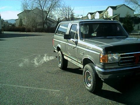 1989 Ford Bronco - A gray Ford Bronco is parked on an asphalt surface, with a plume of exhaust smoke visible.