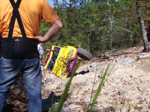 1978 Ford Bronco - Off-road vehicle overturned on a rocky slope, with onlookers present.