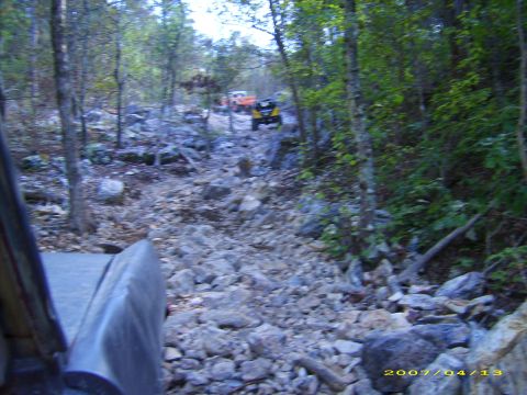 1978 Ford Bronco - Multiple off-road vehicles traverse a challenging, rocky path through a dense forest.