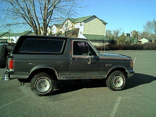 Gray Ford Bronco SUV side profile with hardtop, rear spare tire and all-terrain tires