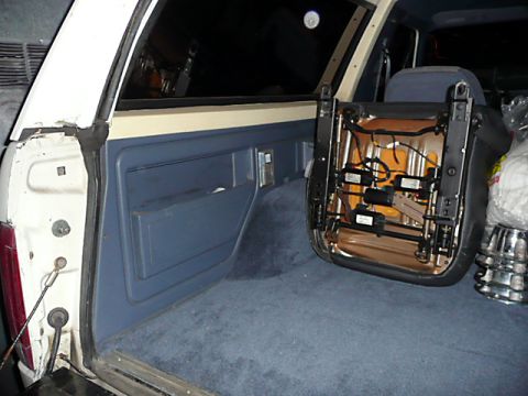 1991 Ford Bronco - The interior of a vehicle shows a removed seat with exposed wiring and mechanisms, sitting on blue carpet.