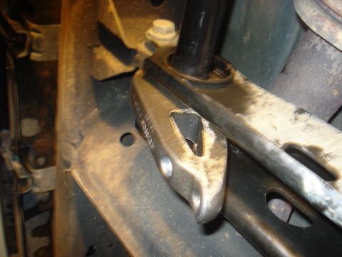 1996 Ford Bronco - Tight underhood detail of a black shock absorber shaft passing through its upper mount on a stamped-steel bracket welded to the frame, with…