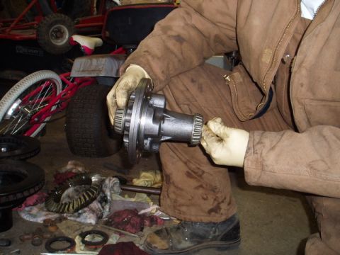 1980 Ford Bronco - A mechanic works on a differential gear assembly, with various automotive parts laid out on the floor.