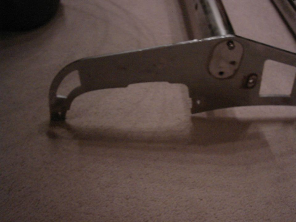 Close-up of a metal bracket with mounting holes, resting on a carpeted surface