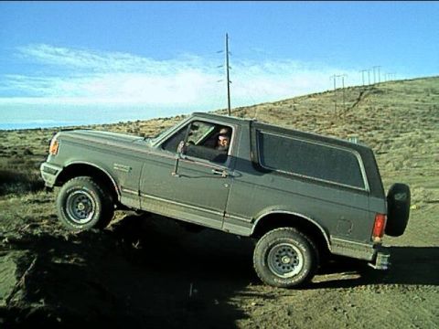 1989 Ford Bronco - A gray Ford Bronco navigates a dirt hill, its off-road capabilities.