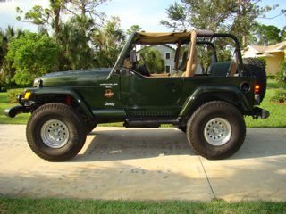 1998 Jeep Wrangler - A green Jeep Wrangler is parked outdoors on a paved surface with trees and a house in the background.
