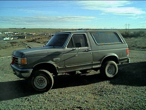 1989 Ford Bronco - This gray Ford Bronco, likely a 1987 model, is parked on a gravel lot under a partly cloudy sky.