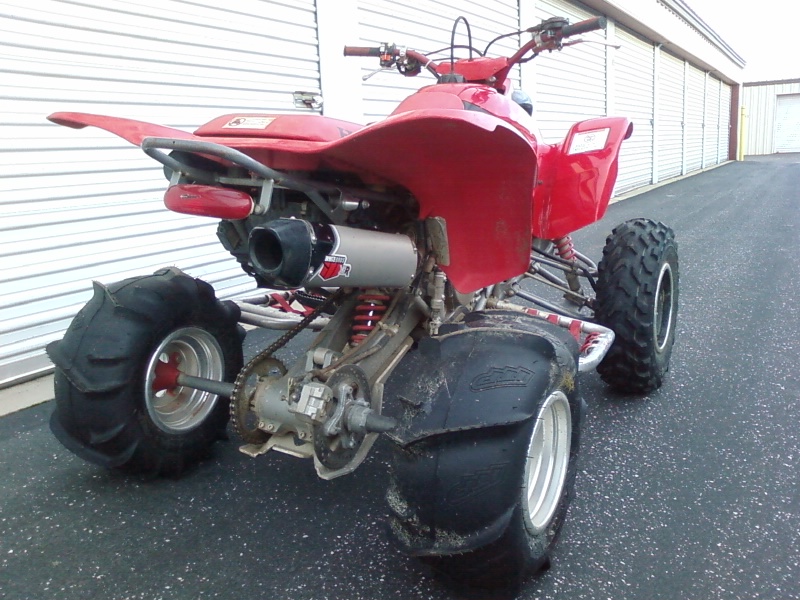 Red ATV with large rear tires and aftermarket exhaust parked in front of a garage