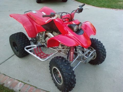 1995 Ford Bronco - A red Honda ATV is parked on a concrete surface with grass in the background.