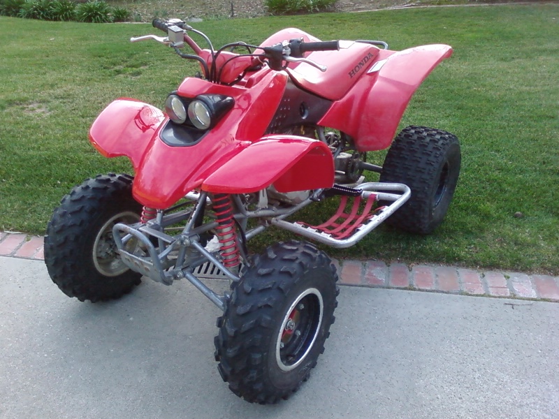 Red ATV with dual headlights and knobby tires parked on concrete