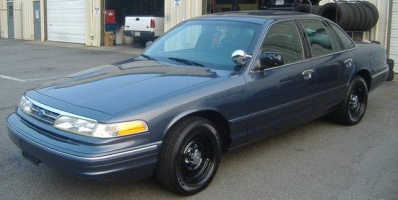 1996 Ford Crown Victoria - A dark blue 1996 Ford Crown Victoria sedan is parked outside a garage with black steel wheels.