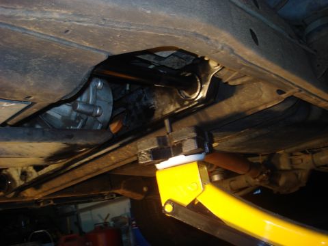 1996 Ford Bronco - Underbody shot of a truck on a yellow floor jack, whose lift pad presses a white puck against a freshly painted black crossmember/skid brac…