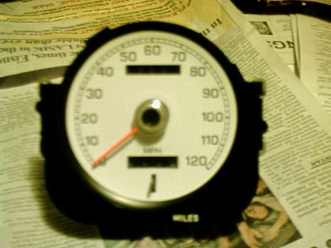 1976 Ford Ranchero - Speedometer gauge with white face and black housing, resting on newspapers.