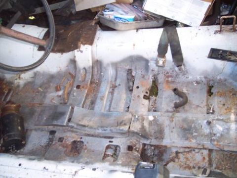 1972 Ford Ranchero - The interior floor of a vehicle shows significant rust and damage, with a steering wheel visible on the left.