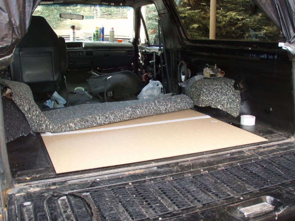 Bare Ford Bronco rear interior with carpet removed and tan floor board laid over the floor pan