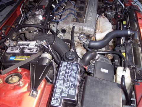 1995 Mitsubishi Eclipse - A view of the engine bay, showing the battery, fuse box, and various engine parts.