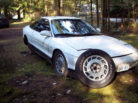 1995 Mitsubishi Eclipse - A white 1991 Ford Probe is parked outdoors, with a spare tire positioned in front of the driver's side wheel well.
