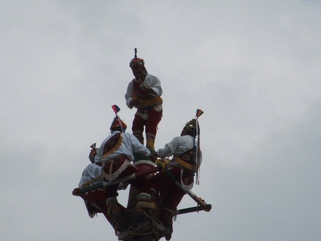 People in traditional costumes performing on a tall structure against a cloudy sky