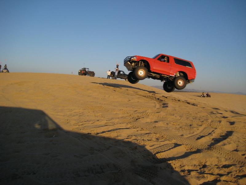 Red SUV airborne over sand dune, front grille guard visible