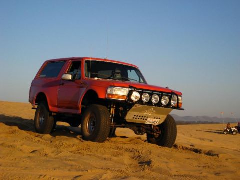 1984 Ford Bronco - This red SUV, likely a 1992-1996 Ford Bronco, is equipped for off-road use with a custom bumper and multiple spotlights.