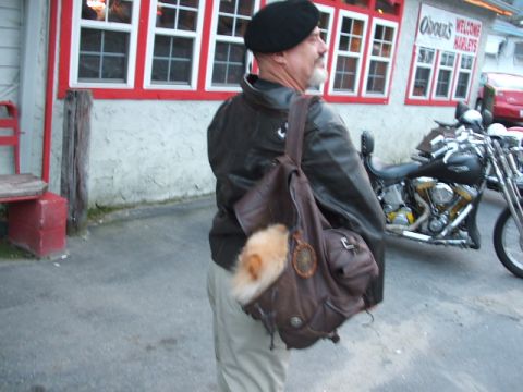 1966 Ford Ranchero - Man with a dog in his backpack stands near a motorcycle outside a building with red trim.