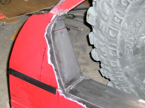 1986 Toyota Hilux - Close-up view of a modified red fender flare and a tire, suggesting bodywork is in progress.
