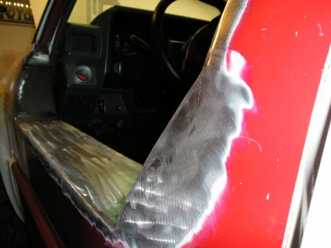 1986 Toyota Hilux - The interior of a red truck shows exposed metal on the door frame during repair, with the steering wheel visible.