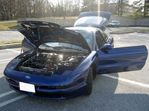 1993 Ford Probe - The engine bay of a blue Ford Probe is visible with the hood and driver's door open.