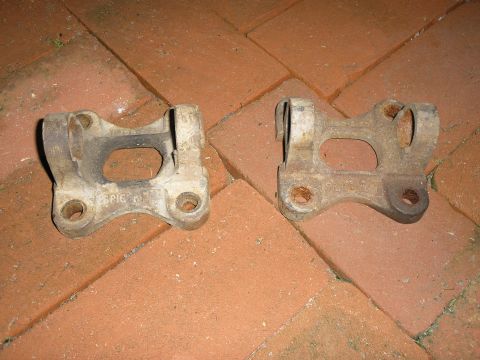 1990 Ford Bronco - Two rusty metal brackets, possibly from a vehicle's suspension system, lie on a brick patio.