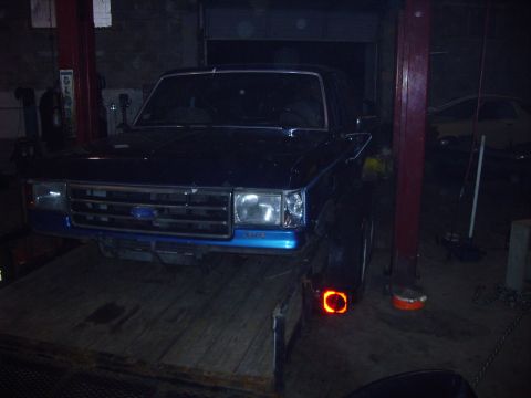 1991 Ford Bronco - A dark blue Ford Bronco is positioned on a trailer in a dimly lit garage.
