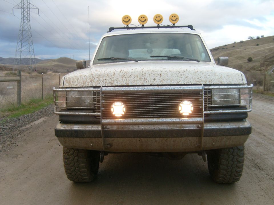Mud-splattered SUV front with brush guard, driving lights and roof-mounted smiley lights