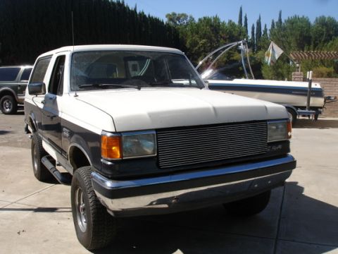 1989 Ford Bronco - This two-tone Ford Bronco is parked in a driveway, with a boat and trailer visible in the background.