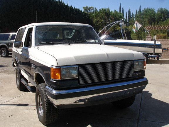 Two-tone Ford Bronco parked in a driveway with a boat trailer behind it