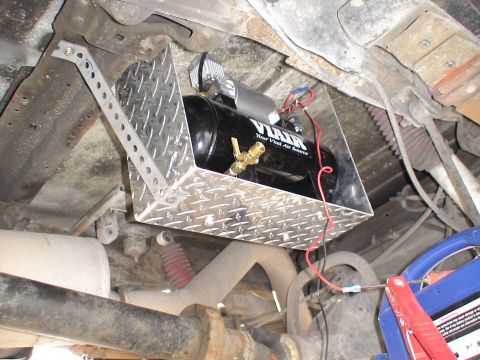 1993 Ford C-350 (Centurion Conversions) - Underside view of a black VIAIR air compressor tank with brass fittings, mounted on a diamond plate bracket.