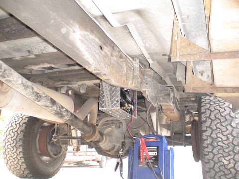 1993 Ford C-350 (Centurion Conversions) - A battery charger is connected to a vehicle's undercarriage, showing the frame, suspension, and exhaust system.
