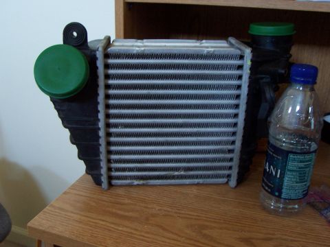 1993 Ford Probe - An intercooler sits on a table next to a bottle of water and other car parts.