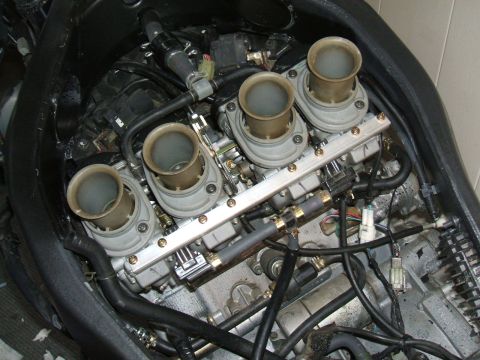 2004 Yamaha FZR600 - Close-up view of motorcycle engine carburetors, showing four intake trumpets and associated fuel lines.