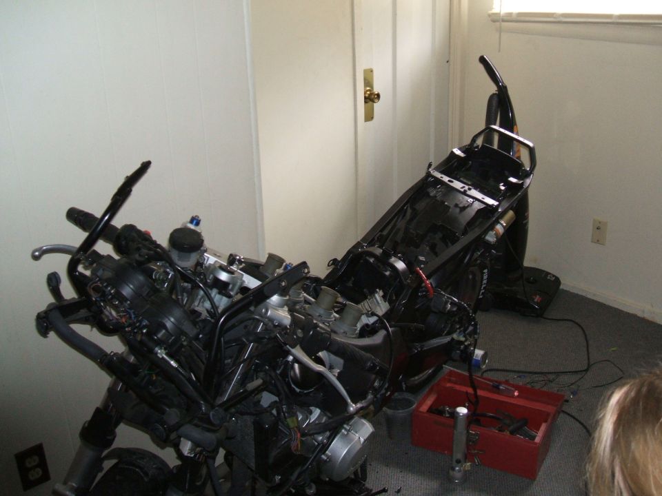 Disassembled motorcycle in a room, with a red toolbox nearby