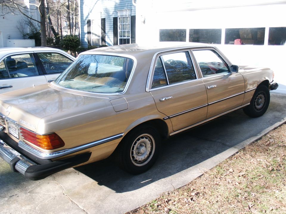 Gold 1970s-80s Mercedes-Benz S-Class sedan parked in a driveway, rear three-quarter view