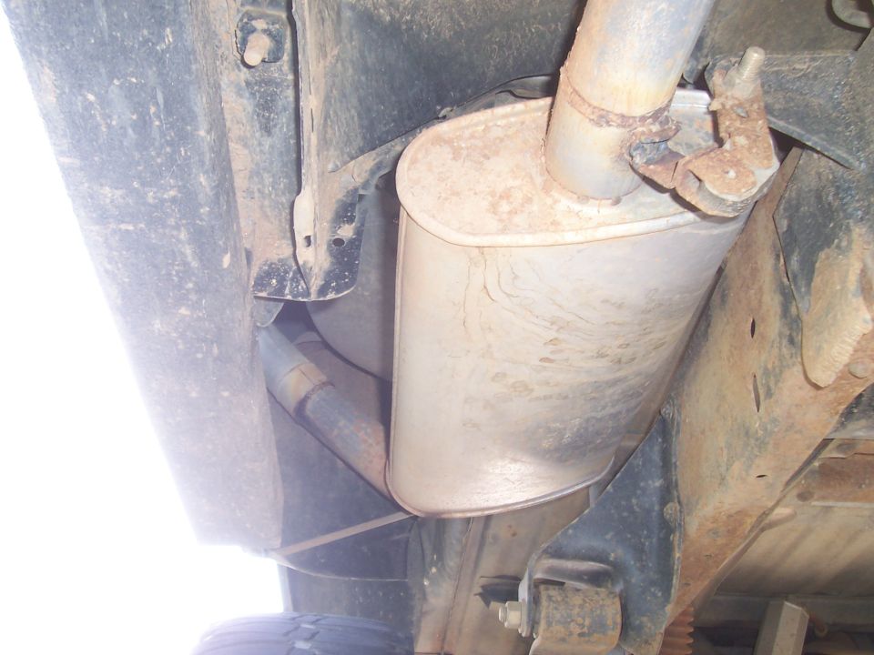 Exhaust muffler and pipes on underside of vehicle, showing rust and dirt