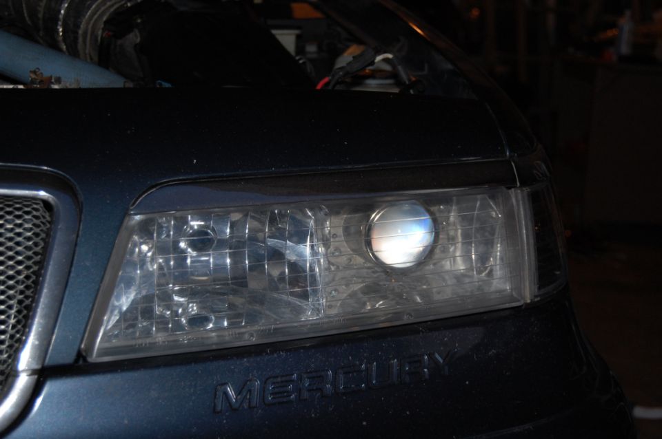 Illuminated projector headlight on dark blue Mercury with chrome badge
