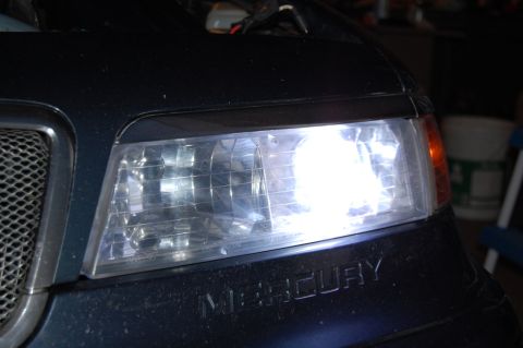1985 Mercury Grand Marquis - A close-up view of a Mercury vehicle's headlight and part of the grille, with the brand name embossed on the body.