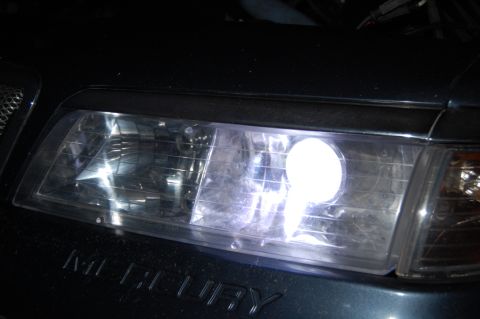 1985 Mercury Grand Marquis - Close-up of a car's headlight assembly, showing a bright LED bulb and the "MERCURY" emblem.