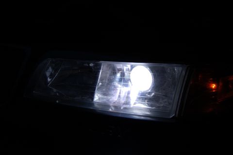 1985 Mercury Grand Marquis - A close-up view of a vehicle's headlight assembly a projector retrofit, illuminated brightly.