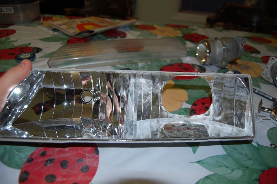 Disassembled chrome headlight housing and lens held over a floral tablecloth