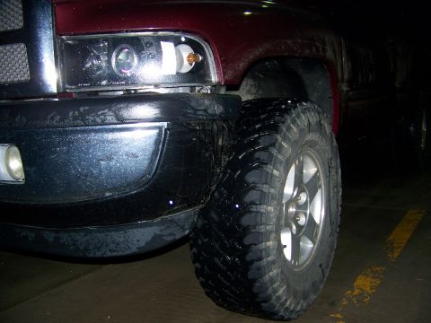 2001 Dodge 1500 - Front corner view of a red 2001 Dodge 1500 pickup truck, large off-road tires and modified headlights.